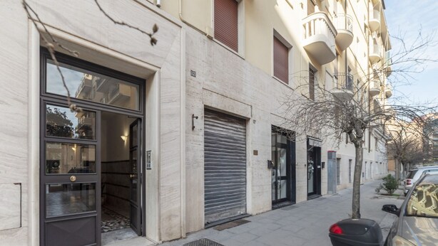Un edificio con ingresso al piano terra, una persiana chiusa e un'auto parcheggiata sul marciapiede.