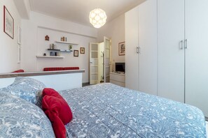 A bedroom with a patterned bedspread, a red pillow, a bedside table, a TV, and a wardrobe.