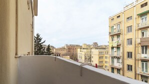 Un balcone con vista su edifici a più piani, un albero e un cielo sereno.