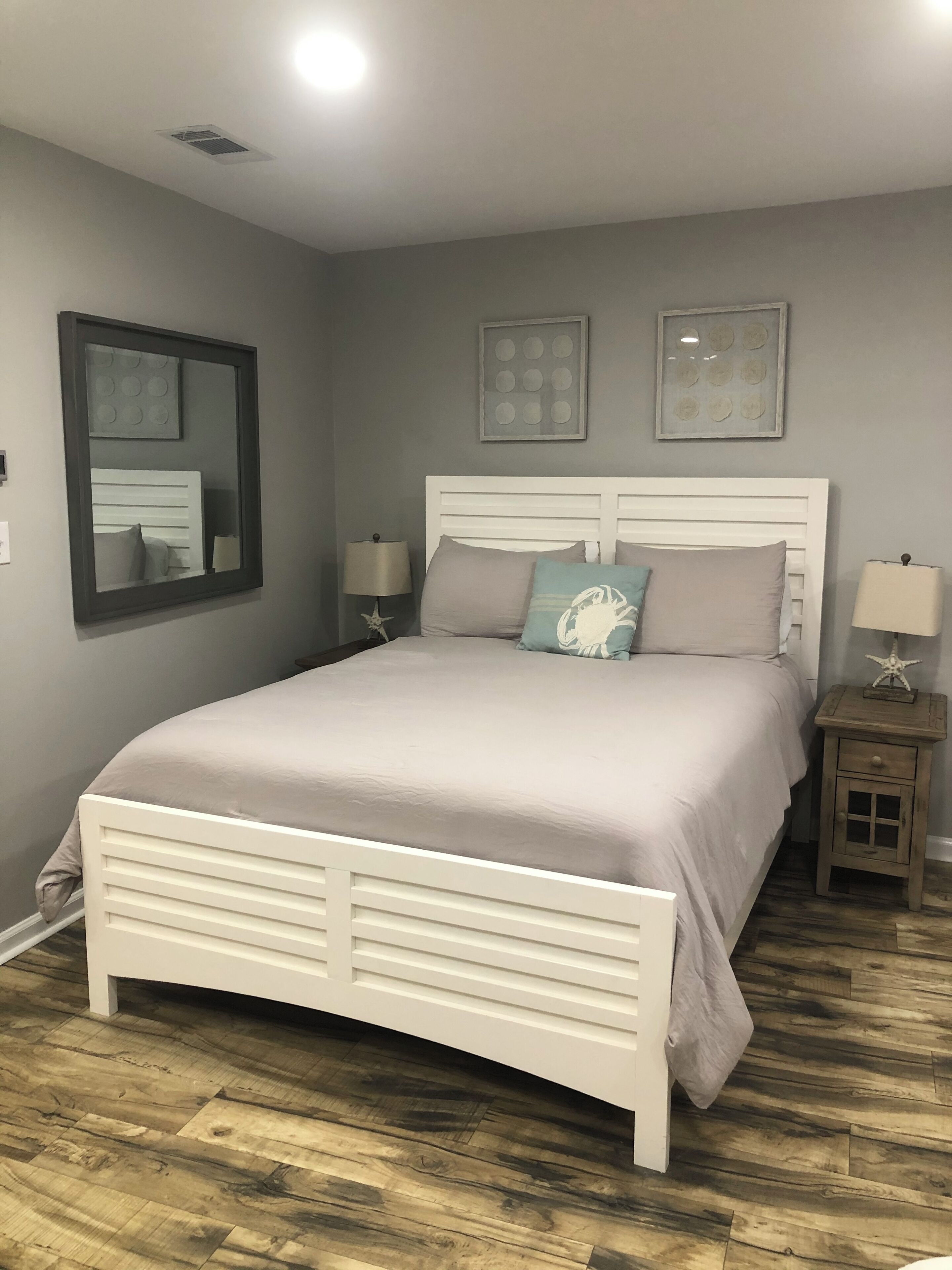 Un dormitorio con cama blanca, paredes grises y suelo de madera.