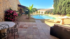 A stone patio with a pool, outdoor seating, and potted plants. - The timeless (Saint-Dionisy)