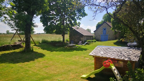 Een rustieke buitenomgeving met een houten speelhuisje, een stenen gebouw en een grasveld.