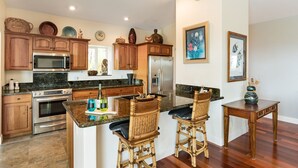 A kitchen with wooden cabinets, a stainless steel refrigerator, a microwave, and a large island with bar stools.