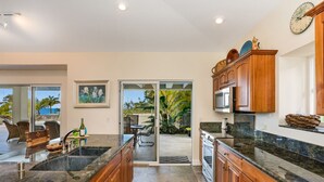 A modern kitchen with granite countertops, wooden cabinets, and a large island. There is a sliding glass door leading to a patio area with outdoor furniture.