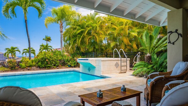 A pool area with a hot tub, lounge chairs, and a view of palm trees.