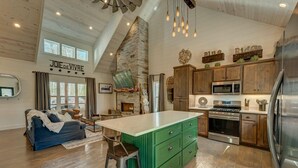 A spacious kitchen with a stone fireplace, wooden cabinets, and modern appliances.
