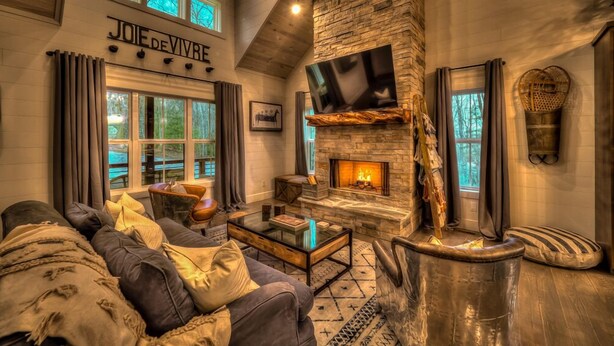 A cozy living room with a stone fireplace, a comfortable sofa, and a television mounted on the wall.
