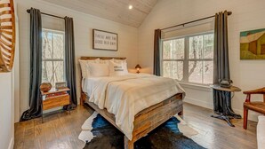 A bedroom with a wooden bed, a nightstand, a lamp, a window with curtains, and a painting on the wall.