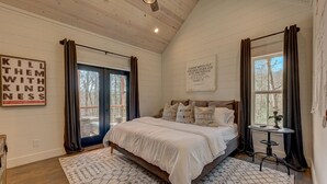 A bedroom with a large bed, a small table, and a view of the outdoors through a window.