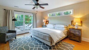 A bedroom with a bed, a nightstand, a chair, a ceiling fan, and a view of the outdoors. - Charming Lakefront Retreat in Palmetto Dunes! (Hilton Head Island)