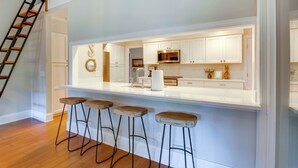 A modern kitchen with white cabinetry, a stainless steel microwave, and a wooden bar stool seating area. - Charming Lakefront Retreat in Palmetto Dunes! (Hilton Head Island)