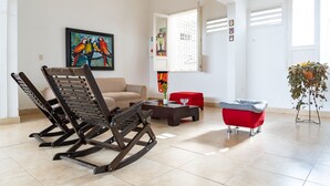 A living room with a rocking chair, a red sofa, a coffee table, and a painting of parrots. - Hotel Villa Ángel (Neiva)
