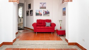 A red sofa in a hallway with tiled flooring and a small table with a plant. - Hotel Villa Ángel (Neiva)