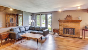 Una sala de estar moderna con un sofá seccional, una mesa de centro de madera, una chimenea y ventanas grandes.