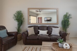 A living room with a brown leather sofa, two potted plants, a woven basket, and a mirror on the wall.