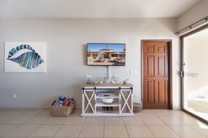 A room with a tiled floor, a wooden door, a white cabinet with shelves, a framed picture, and a wall-mounted television.