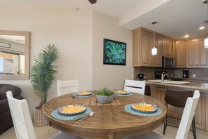 A dining area with a round wooden table, white chairs, and a potted plant.