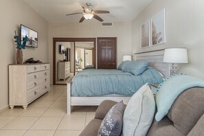 A bedroom with a bed, a dresser, a ceiling fan, and a door leading to another room.