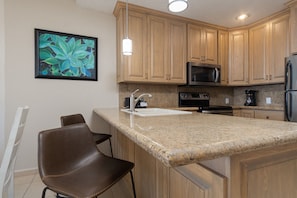 A kitchen with wooden cabinets, a granite countertop, a stainless steel refrigerator, a microwave, a stove, and a coffee maker.