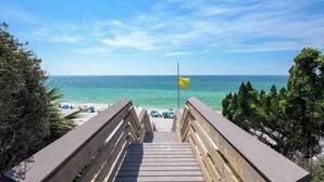 A wooden boardwalk leading to a beach with a flag, clear sky, and ocean view.