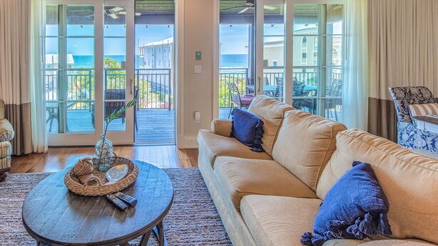 A living room with a sofa, a coffee table, and a view of the ocean through large sliding glass doors.