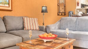 Un salon avec deux canapés gris, une table basse en bois sur laquelle se trouve un saladier rempli de fruits, et deux coupes à champagne.