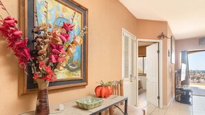 Une pièce avec une table, un vase de fleurs, un tableau et une vue sur la mer, visible à travers une porte.
