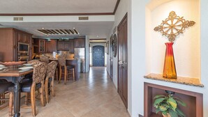 A spacious kitchen with modern appliances, a dining area with wooden chairs, and a decorative wall piece. - Sonoran Sky 1403 Exquisite Spacious Ocean View Condo (Puerto Peñasco)