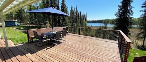 Una terraza de madera con mesa y sillas, con vistas a un lago y un bosque.