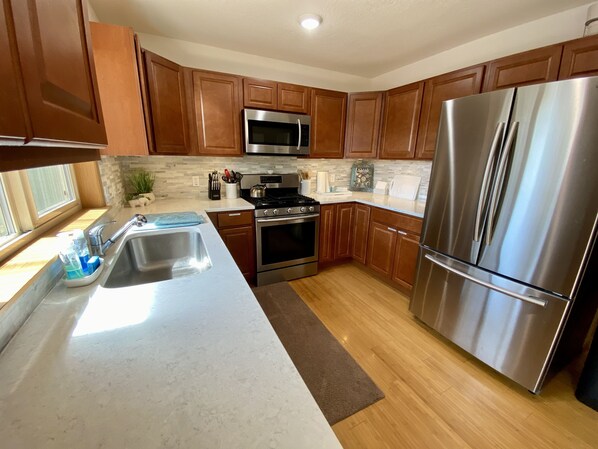A modern kitchen with wooden cabinets, stainless steel appliances, a microwave, stove, oven, and a refrigerator. - Lakefront Home next to Kenai and Kasilof River. Sleeps 10 (Kasilof)