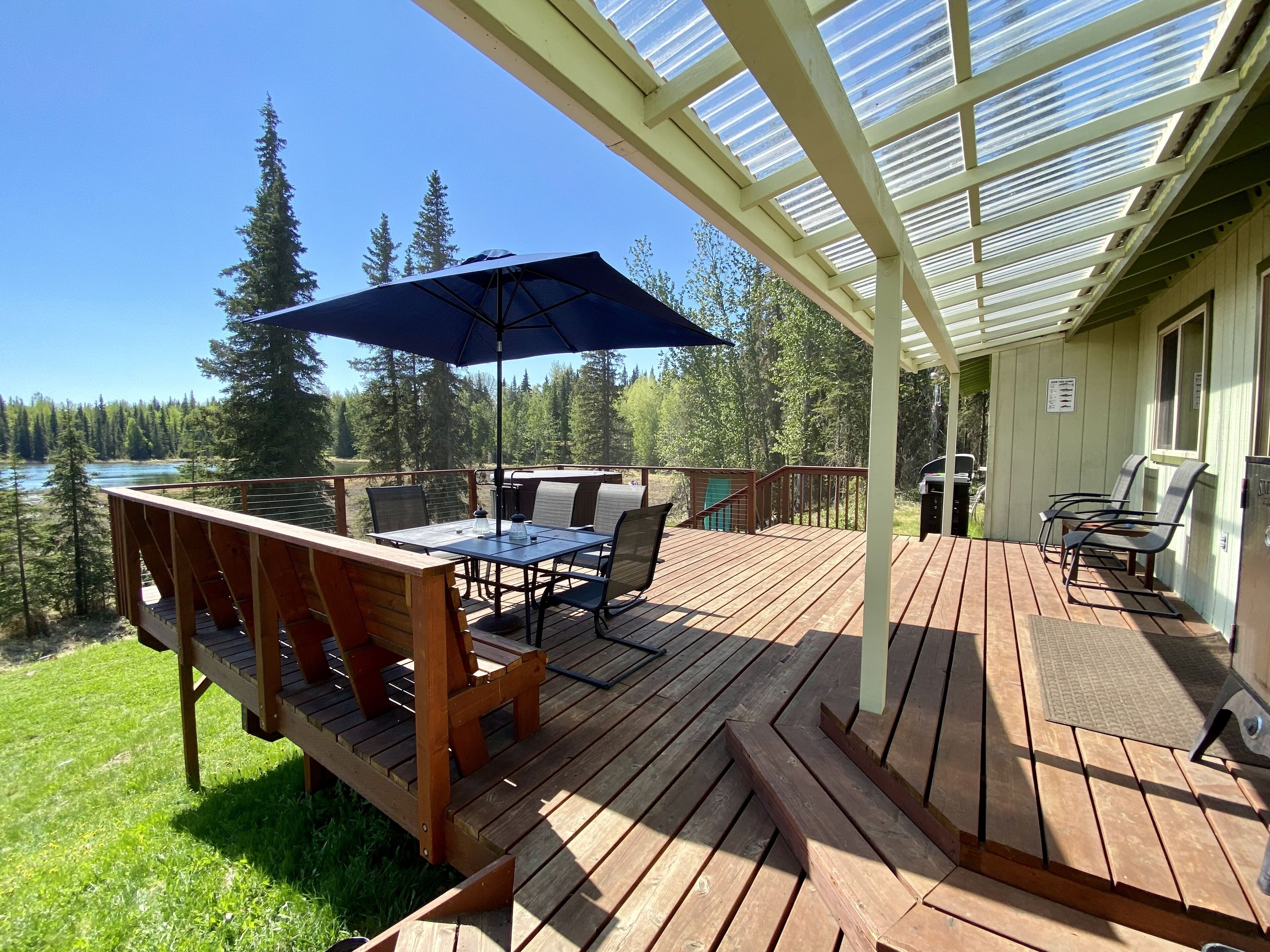 Una terraza de madera con mobiliario exterior, una mesa y una sombrilla.