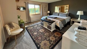 Een slaapkamer met een bed, nachtkastjes, een stoel, een bureau, een vloerkleed en een raam met gordijnen.