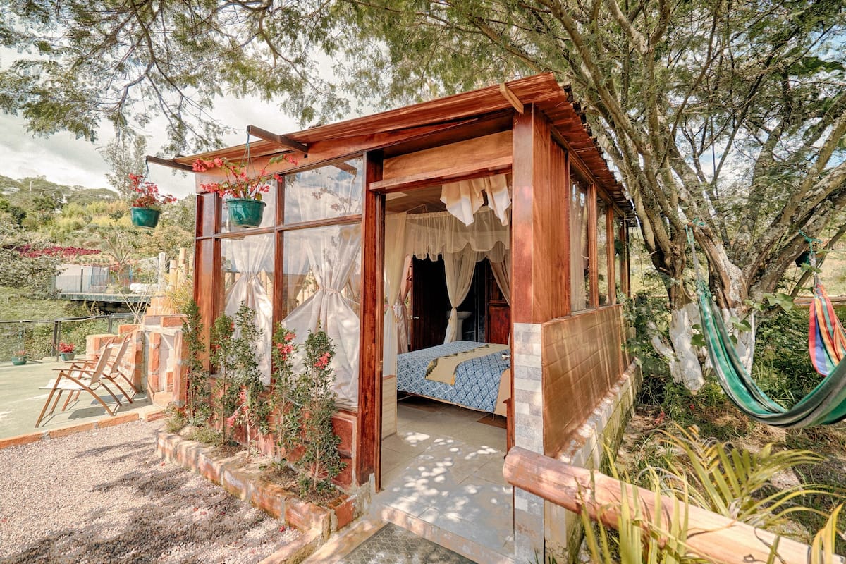Eine rustikale Holzhütte mit einem Bett, einer Hängematte und Topfpflanzen.