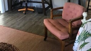 A living room with a desk, a pink chair, a round mirror, and a clock on the wall. - Relaxing Getaway on Florida's St Johns River! (Astor)