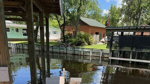 A wooden dock extending over a calm water body, surrounded by greenery and residential buildings. - Relaxing Getaway on Florida's St Johns River! (Astor)