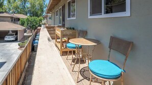 Une terrasse extérieure couverte, avec une table et des chaises, une clôture en bois et une voiture garée au fond.