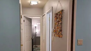 Un couloir doté d’un plancher en bois, d’un objet décoratif fixé au mur et d’une porte donnant sur une autre pièce.
