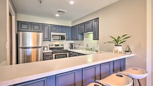 Una cocina moderna con armarios oscuros, electrodomésticos de acero inoxidable y una barra con taburetes.