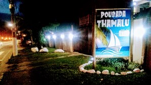 A nighttime view of a sign for Pousada Thamalu with a sailboat graphic, surrounded by rocks and minimal lighting. - Pousada Thamalu 228 (Paraty)