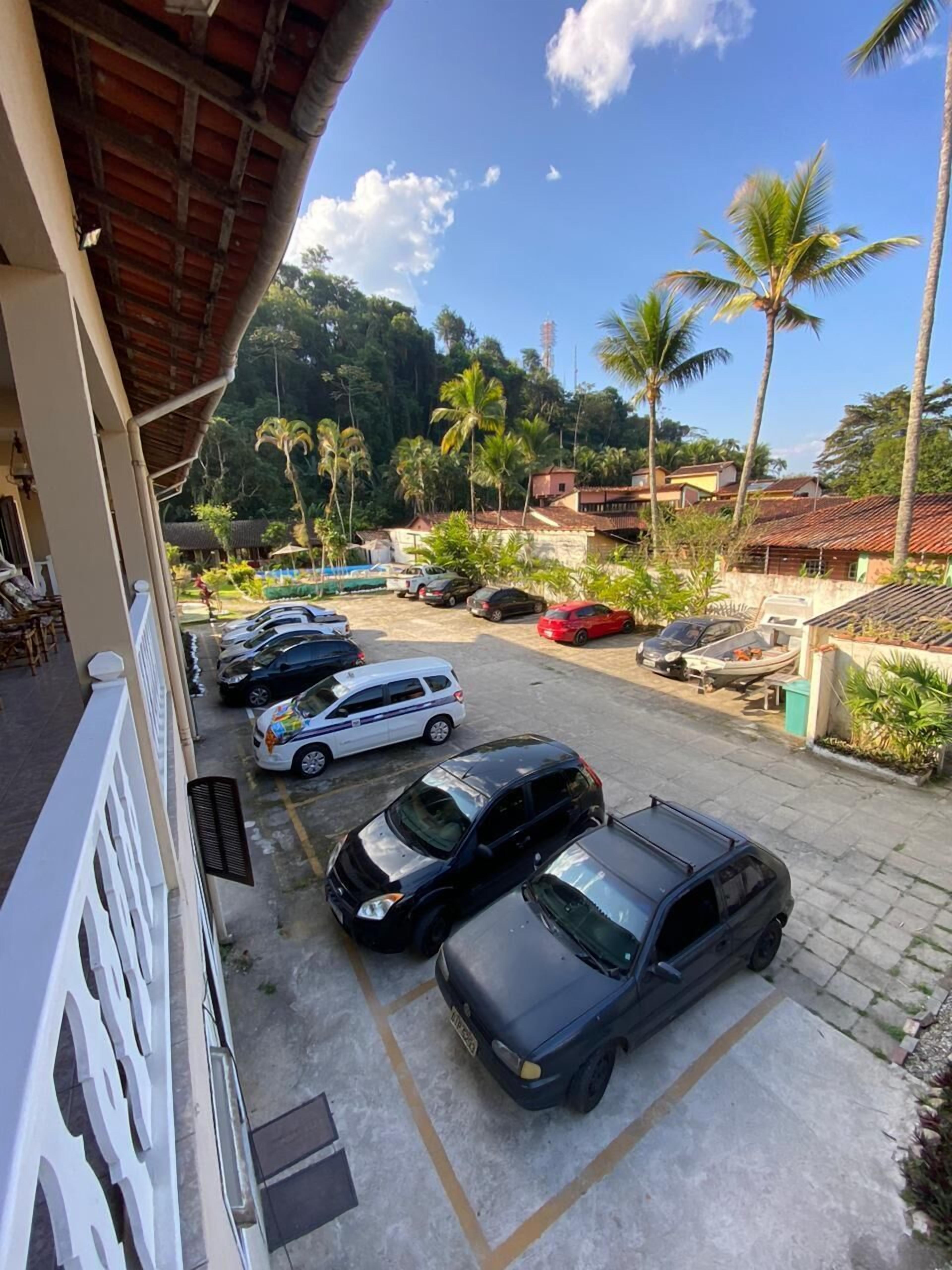 A parking area with several cars, a building with a tiled roof, and palm trees in the background.