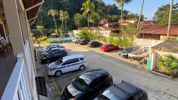 A parking area with several cars, a building with a tiled roof, and palm trees in the background.