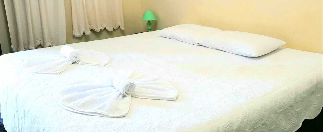 Una cama bien hecha con sábanas blancas y dos toallas dobladas en forma de lazo.