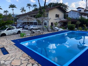 A swimming pool with a blue border, surrounded by lounge chairs and umbrellas. - Pousada Thamalu 228 (Paraty)