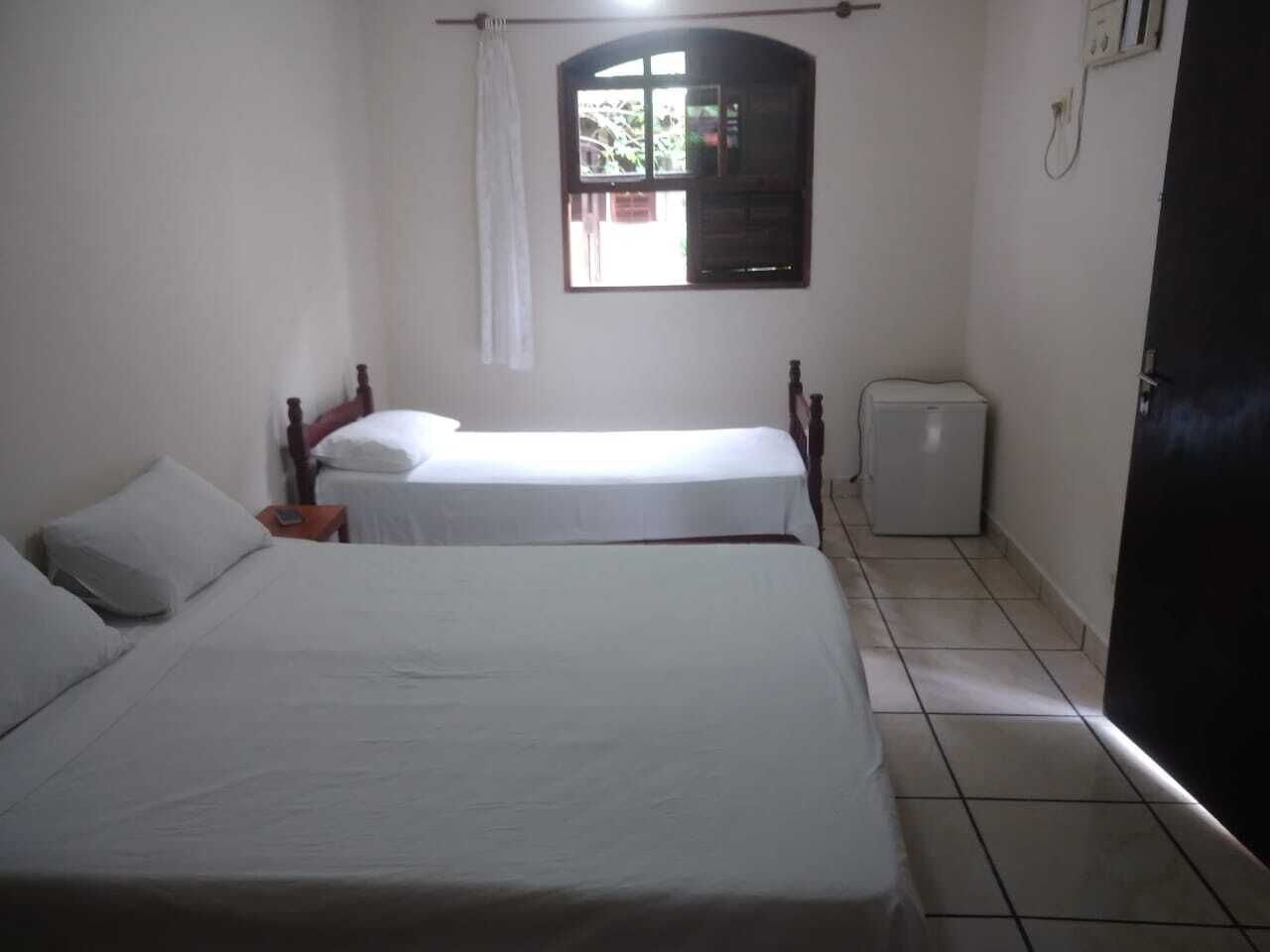 A room with two beds, a window, a small refrigerator, and a door.