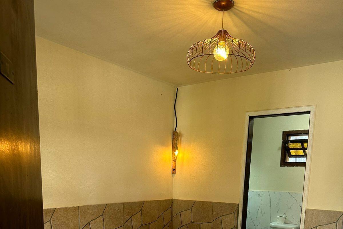 A hotel room with a bed, a wall-mounted light fixture, a bathroom visible through a door, and a stone-patterned wall.