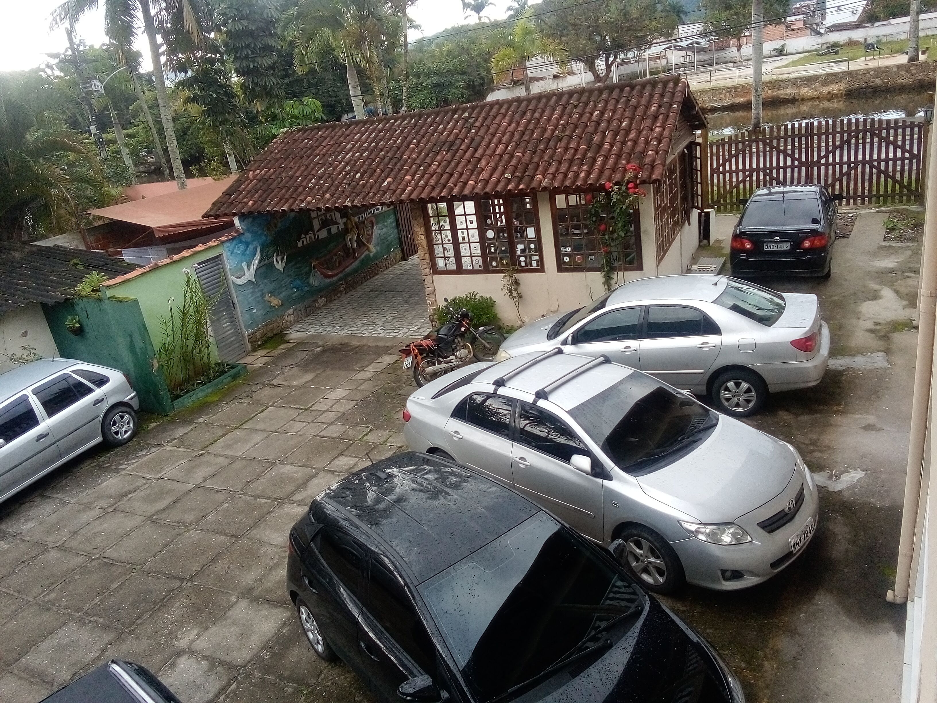 A parking area with several cars, a small building with a tiled roof, and a mural on the wall.