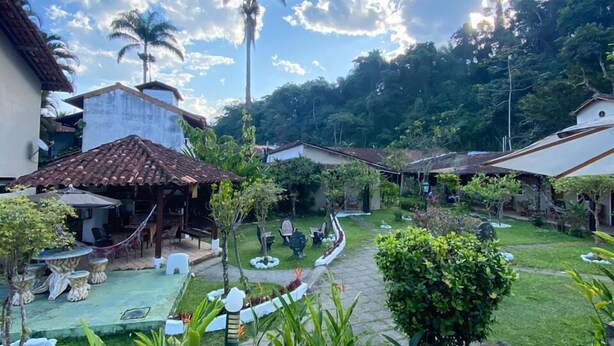 A courtyard with outdoor seating, palm trees, and stone pathways. - Pousada Thamalu 228 (Paraty)