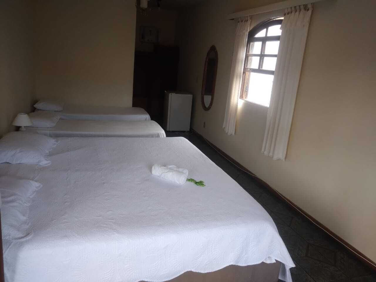 A hotel room with three beds, a small refrigerator, and a window with curtains.