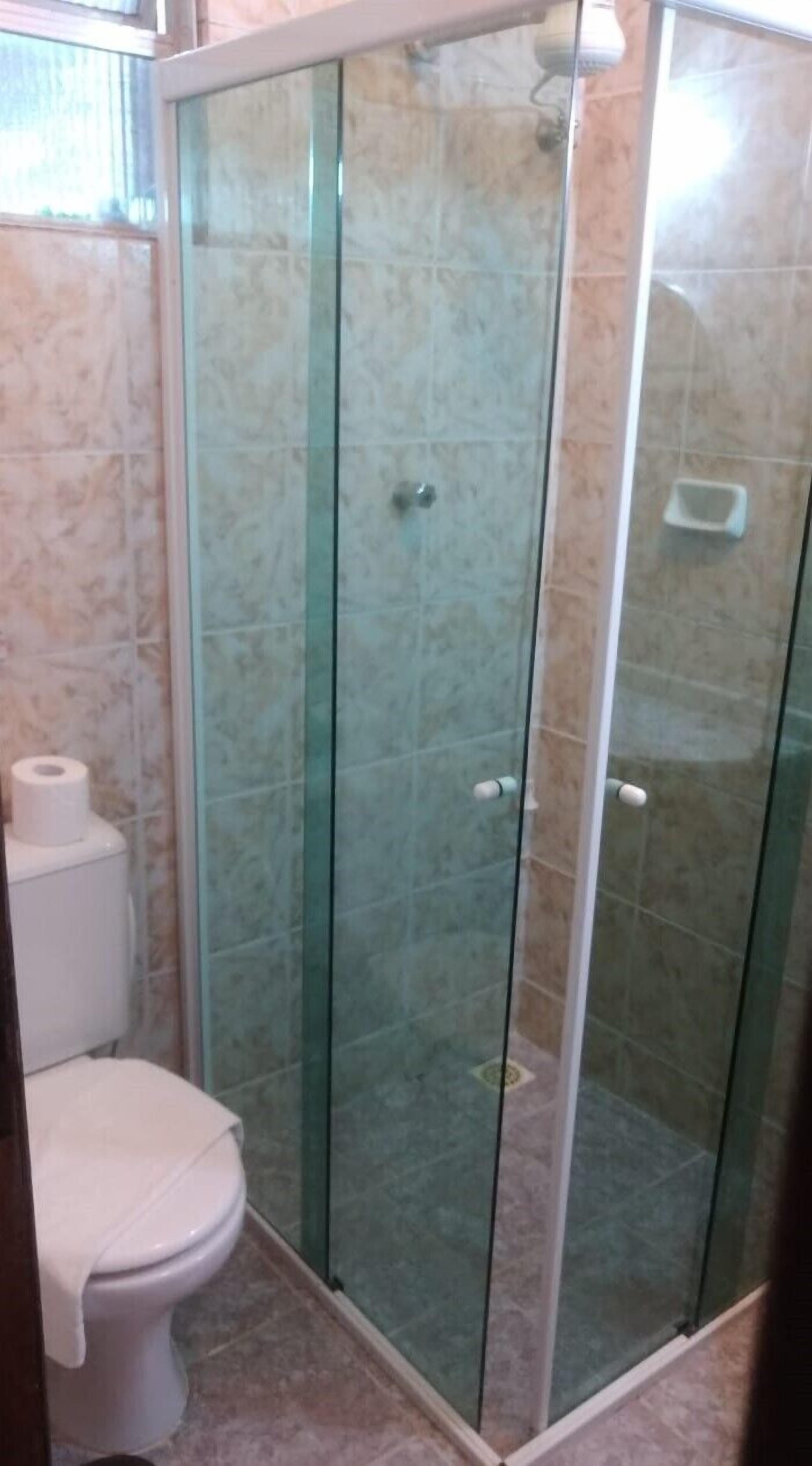 A bathroom with a glass-enclosed shower, a toilet, and a marble-tiled floor.
