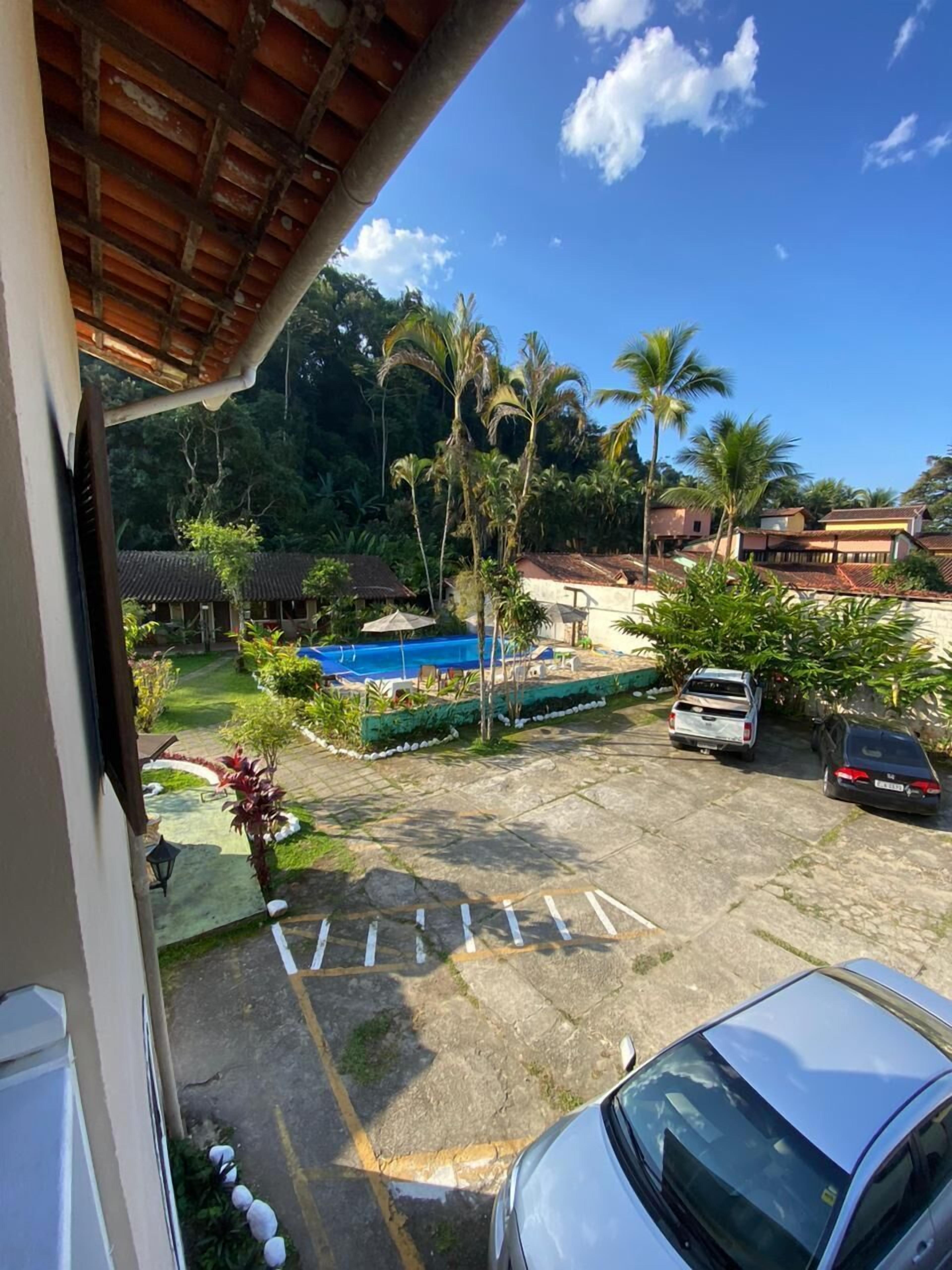 A view from a balcony overlooking a parking area with a pool, palm trees, and a clear blue sky.